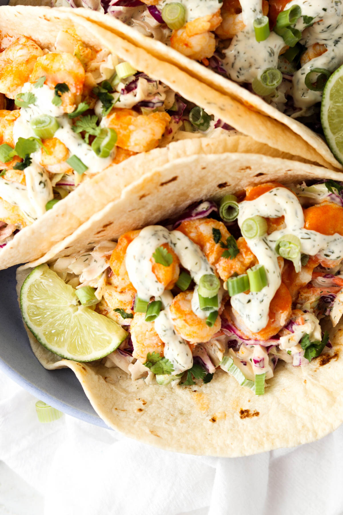 Buffalo shrimp tacos on a blue plate with coleslaw and green onions.