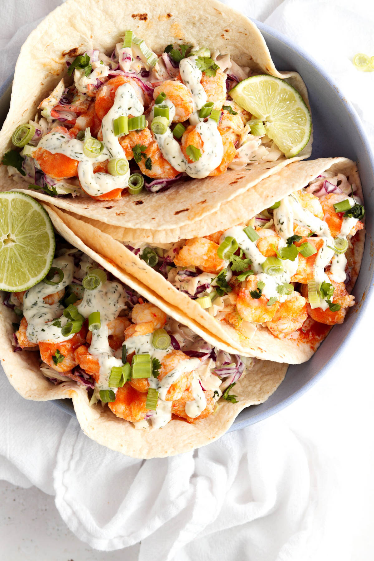 Three buffalo shrimp tacos on a plate garnished with fresh lime and green onions.