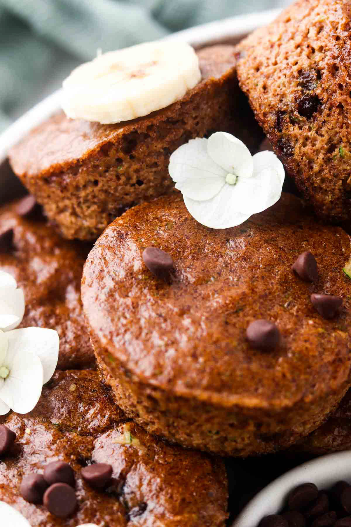 Gluten free zucchini muffins on a plate with dairy free chocolate chips and fresh banana slices. 