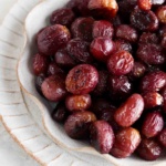 Roasted grapes on a ruffled off white plate.