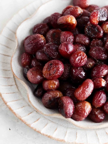 Roasted grapes on a ruffled off white plate.