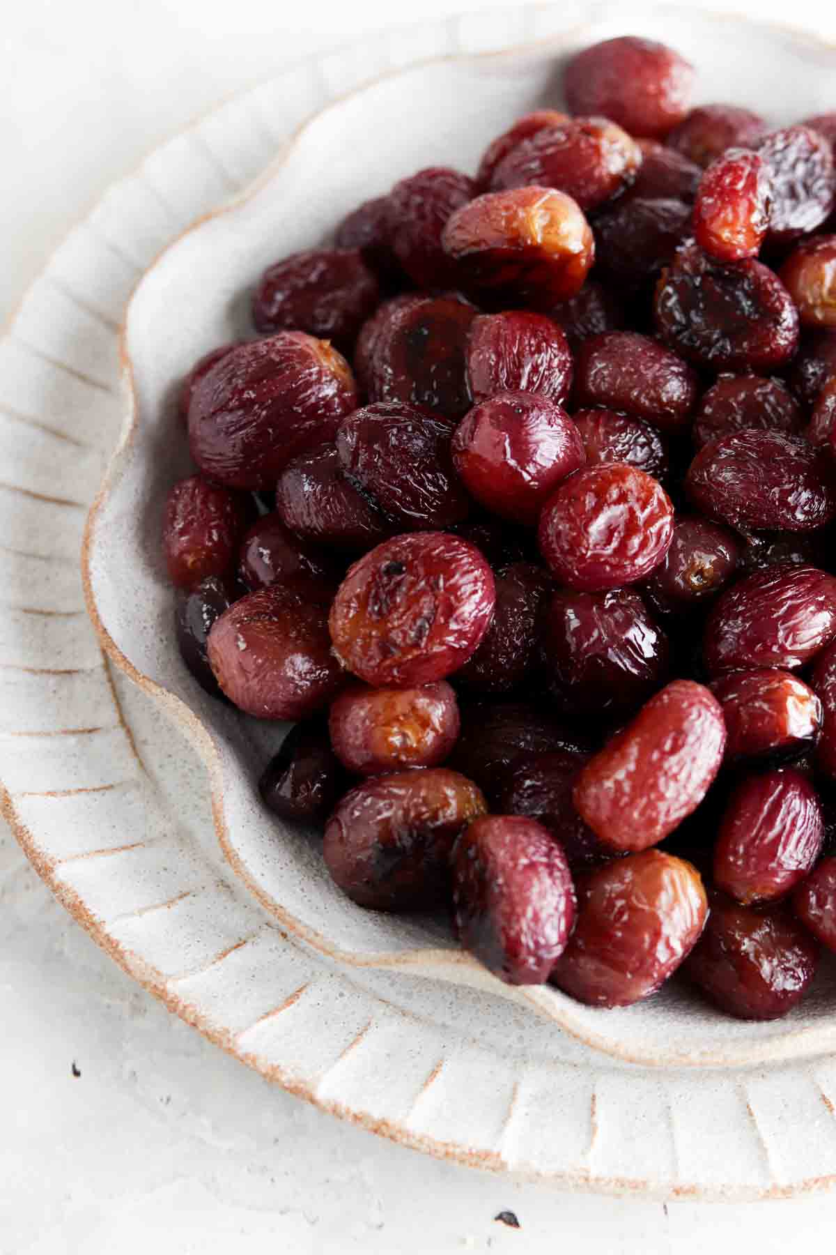 Roasted grapes on a ruffled off white plate.