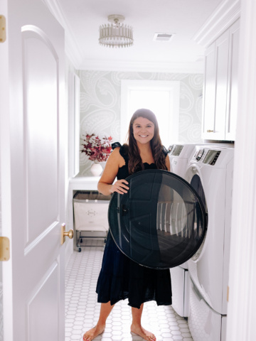 Allianna moximchalk in a black dress standing inside her laundry room.
