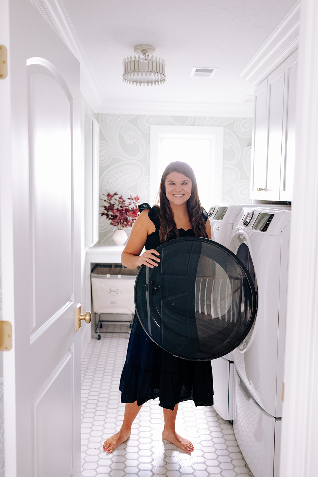 Allianna moximchalk in a black dress standing inside her laundry room.