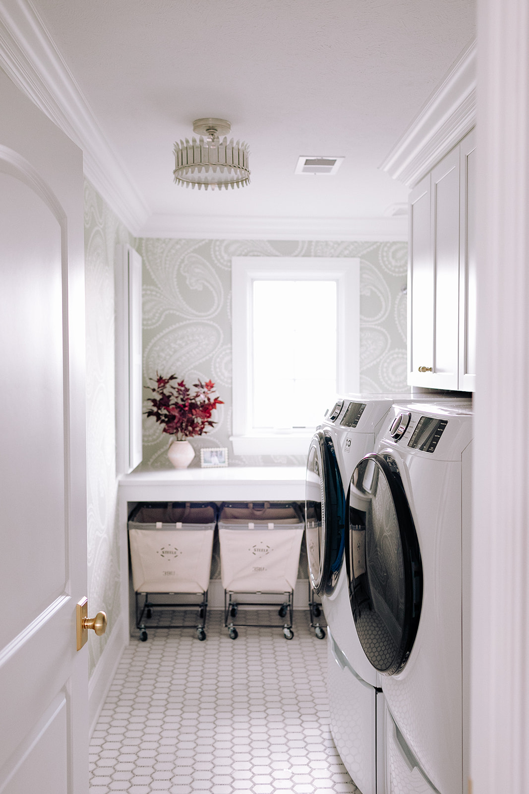 Stunning laundry room with white washer and dryer, pink plant and light green wallpaper.