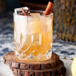 Clear glass with a brown drink and a cinnamon stick in it.