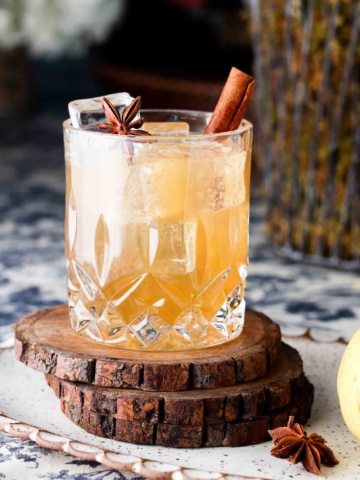 Clear glass with a brown drink and a cinnamon stick in it.