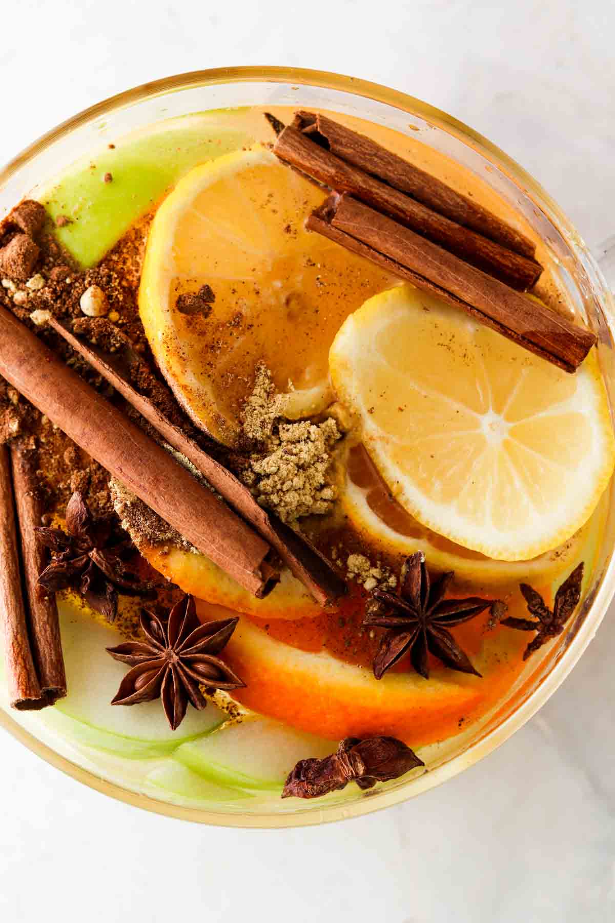 Spices, lemons, oranges, and apples in a large glass pot.