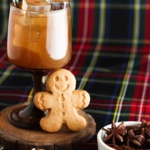 Gingerbread cocktail in a brown glass with bells on top and a gingerbread man standing next to the cup.