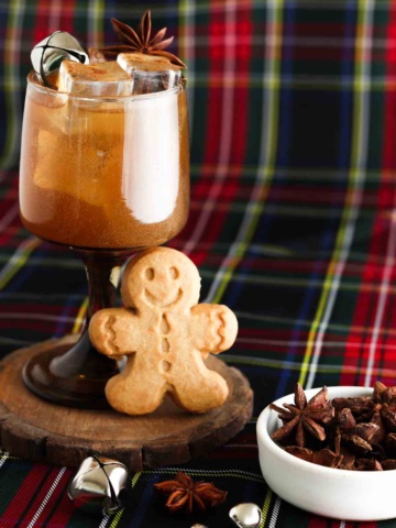 Gingerbread cocktail in a brown glass with bells on top and a gingerbread man standing next to the cup.