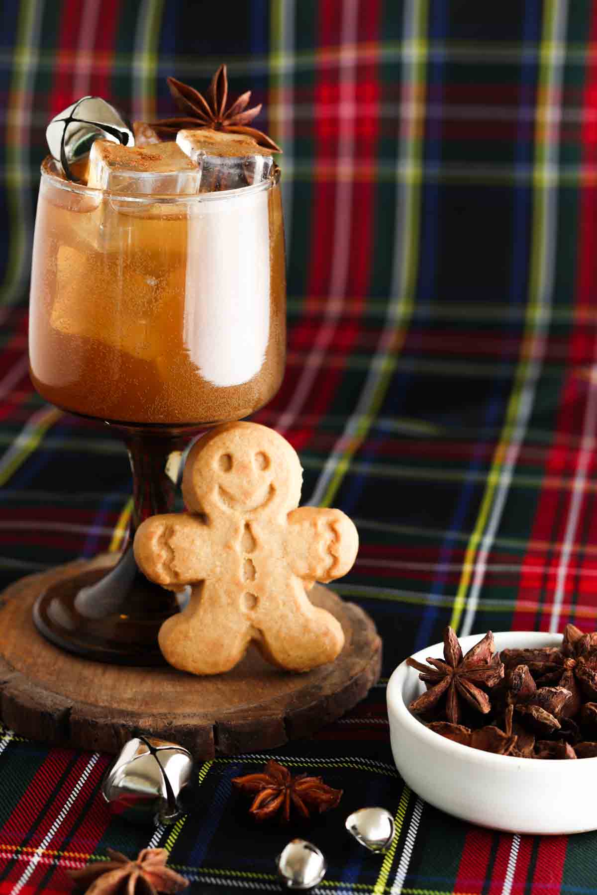 Gingerbread cocktail in a brown glass with bells on top and a gingerbread man standing next to the cup. 