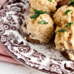 Stuffed mushrooms on a brown and white plate with fresh parsley on top.
