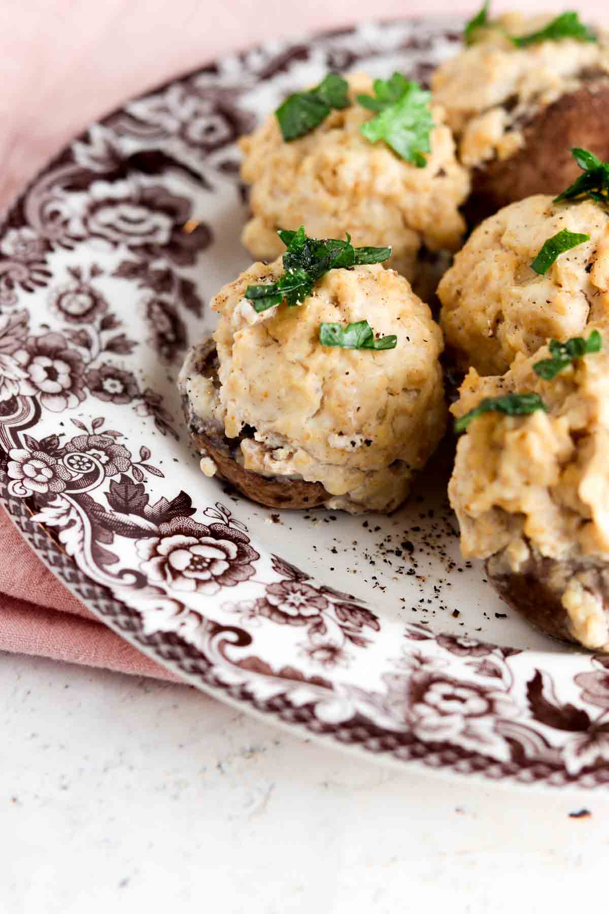 Stuffed mushrooms on a brown and white plate with fresh parsley on top.
