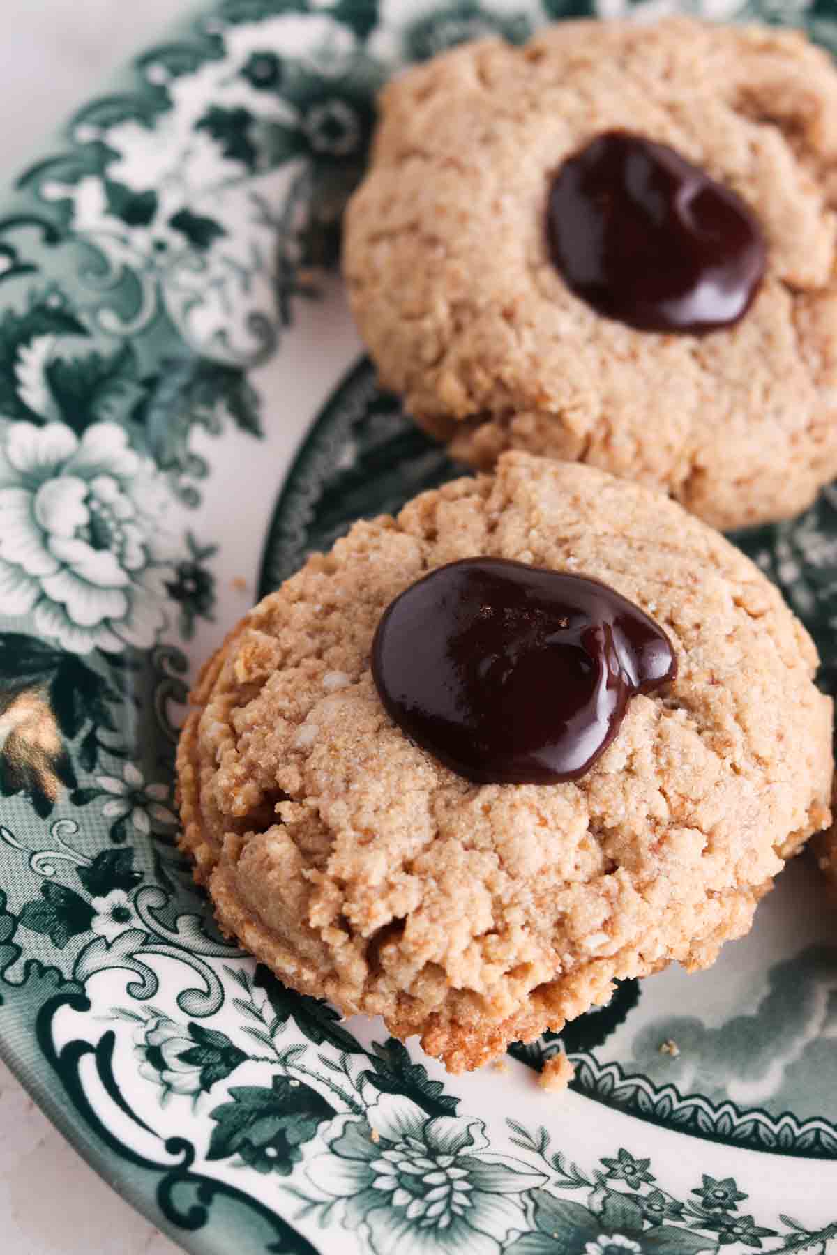 Thumbprint cookies on a green and white plate with chocolate ganache in the middle.