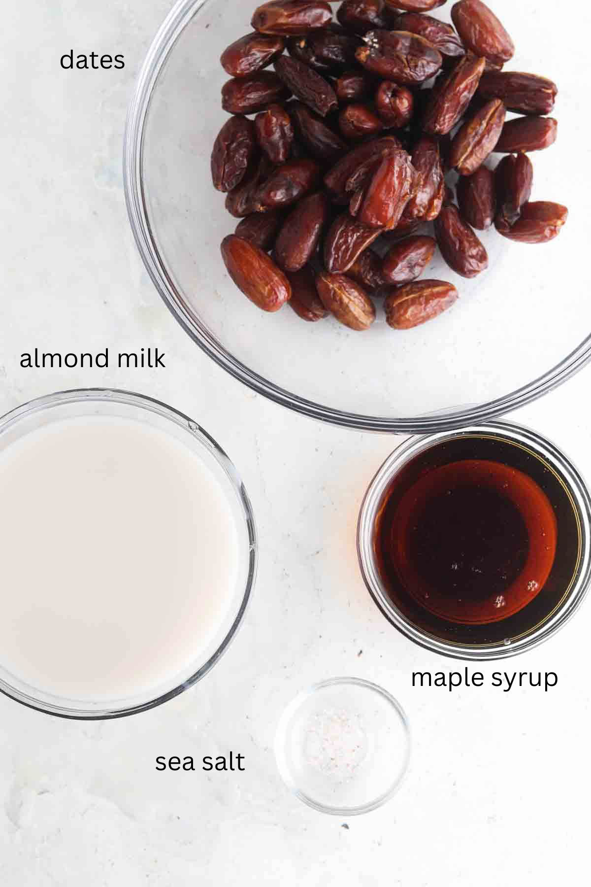 Date, coconut milk, maple syrup and salt sitting out in glass bowls. 