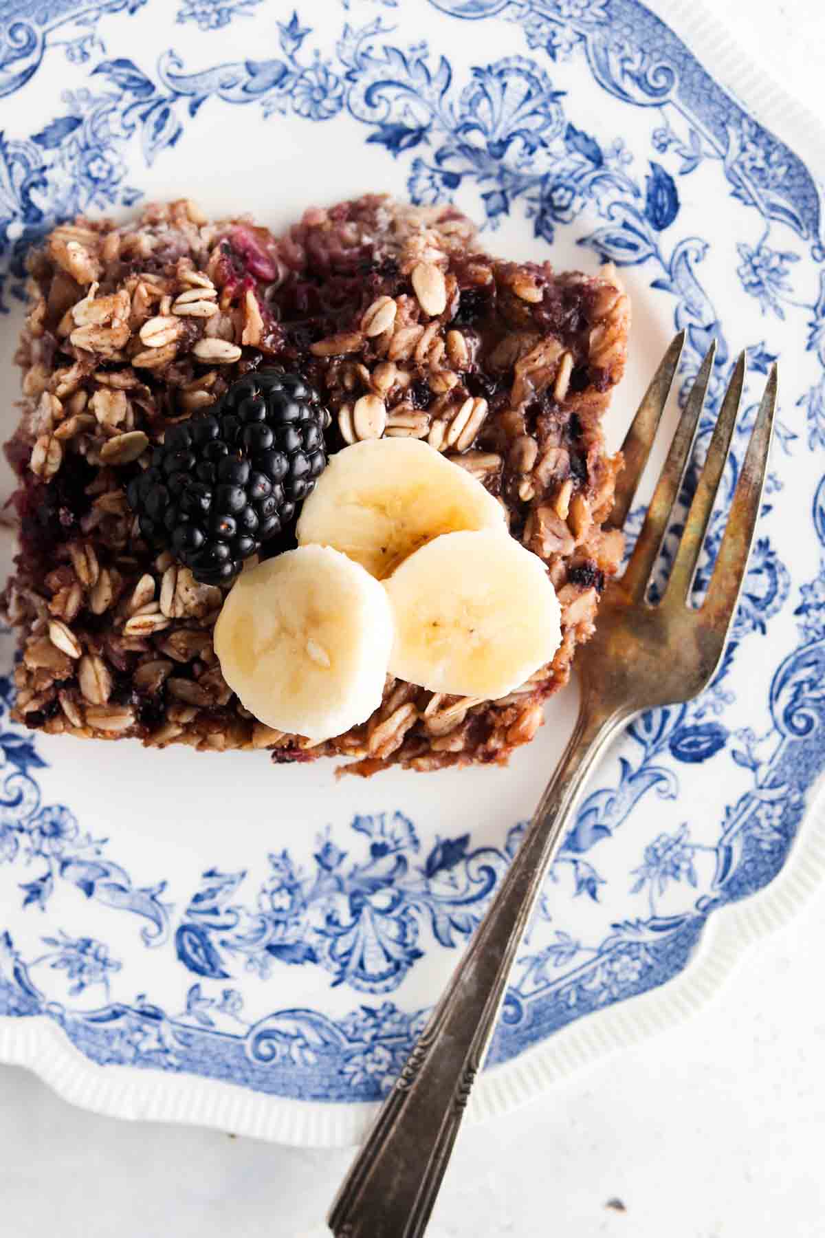 Blackberry baked oatmeal on a blue plate with banana slices and blackberries.