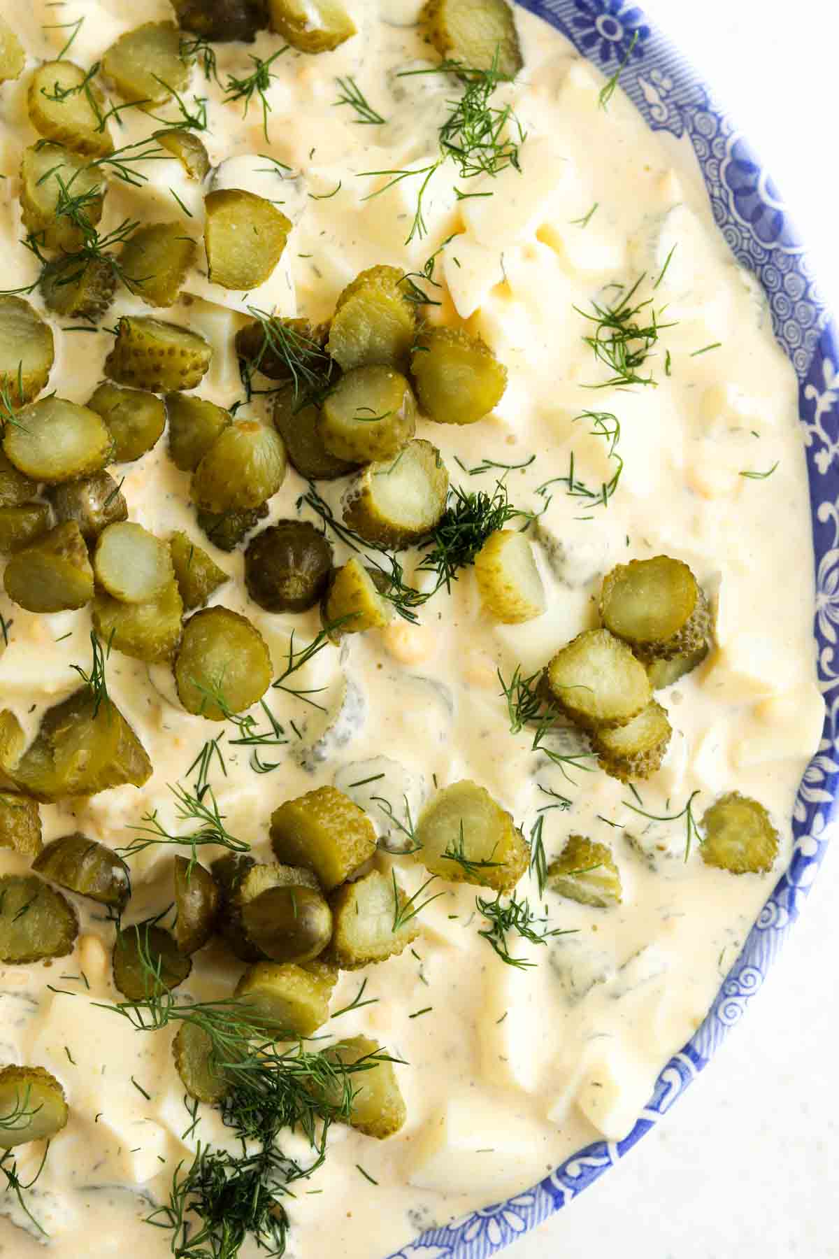 Egg salad in a large blue bowl with pickles and fresh dill on top.