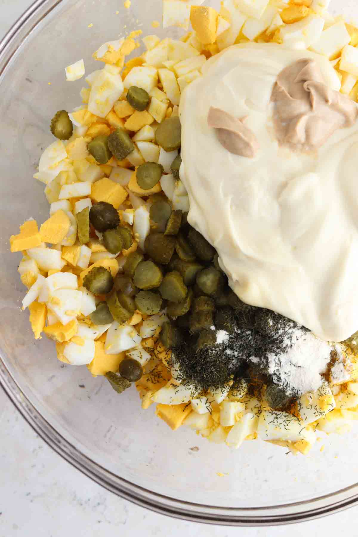 Egg salad ingredients mixed tossed together in a large glass bowl.