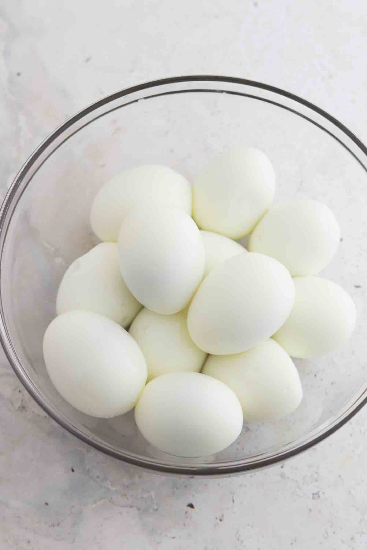 Peeled hard boiled eggs in a glass bowl.