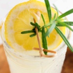 Overhead picture of lemonade in a glass with a lemon and sprig of rosemary on top.