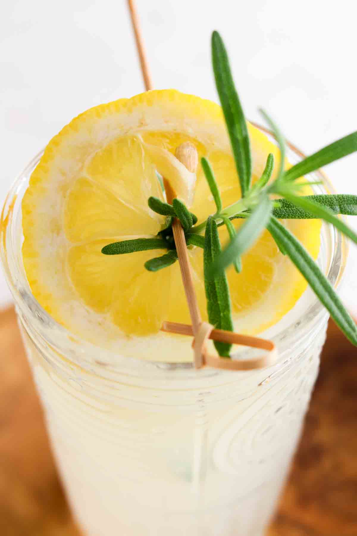 Overhead picture of lemonade in a glass with a lemon and sprig of rosemary on top.