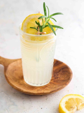 Glass of lemonade in a cup with lemon and rosemary on top.
