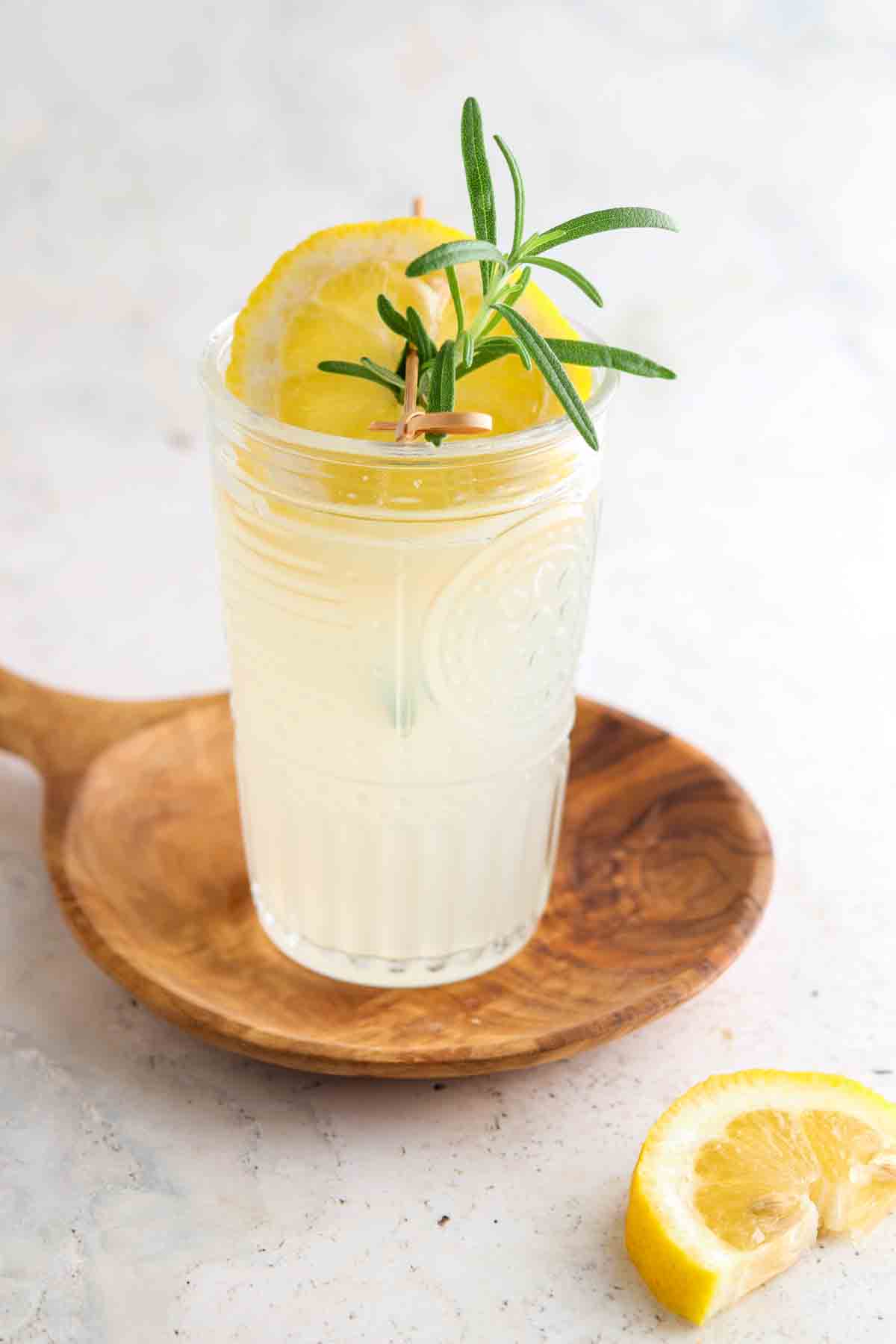 Glass of lemonade in a cup with lemon and rosemary on top.