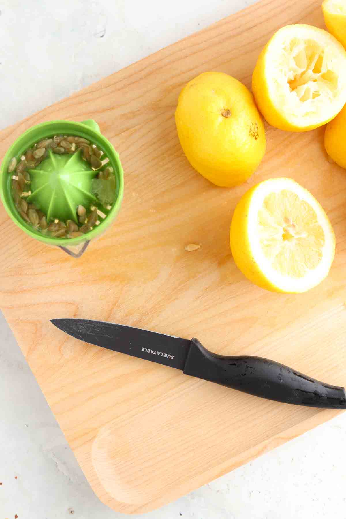 Juiced lemons on the cutting board with a knife and juicer.