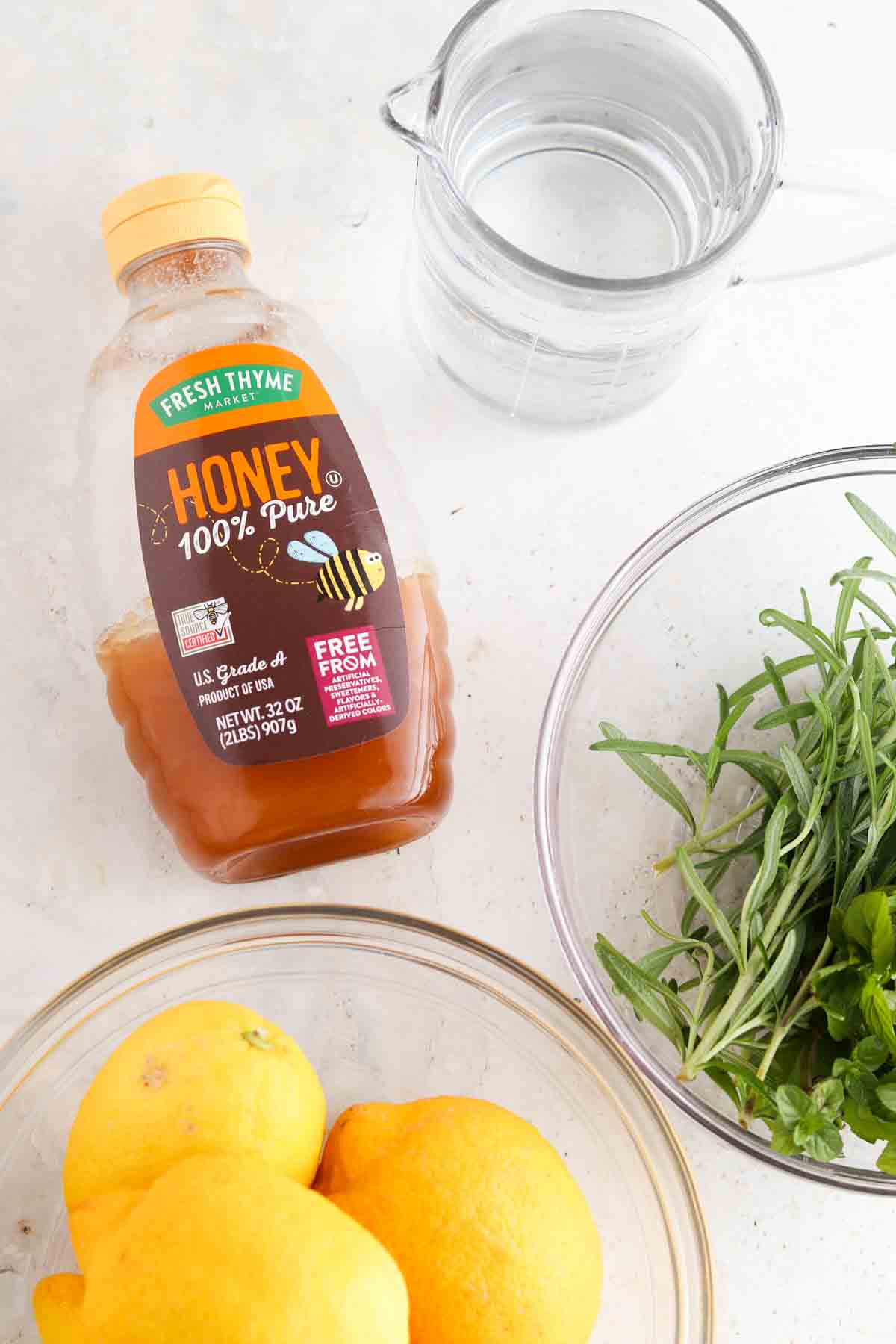 Honey, lemons, water, rosemary and mint in small glass bowls sitting on the coutner. 