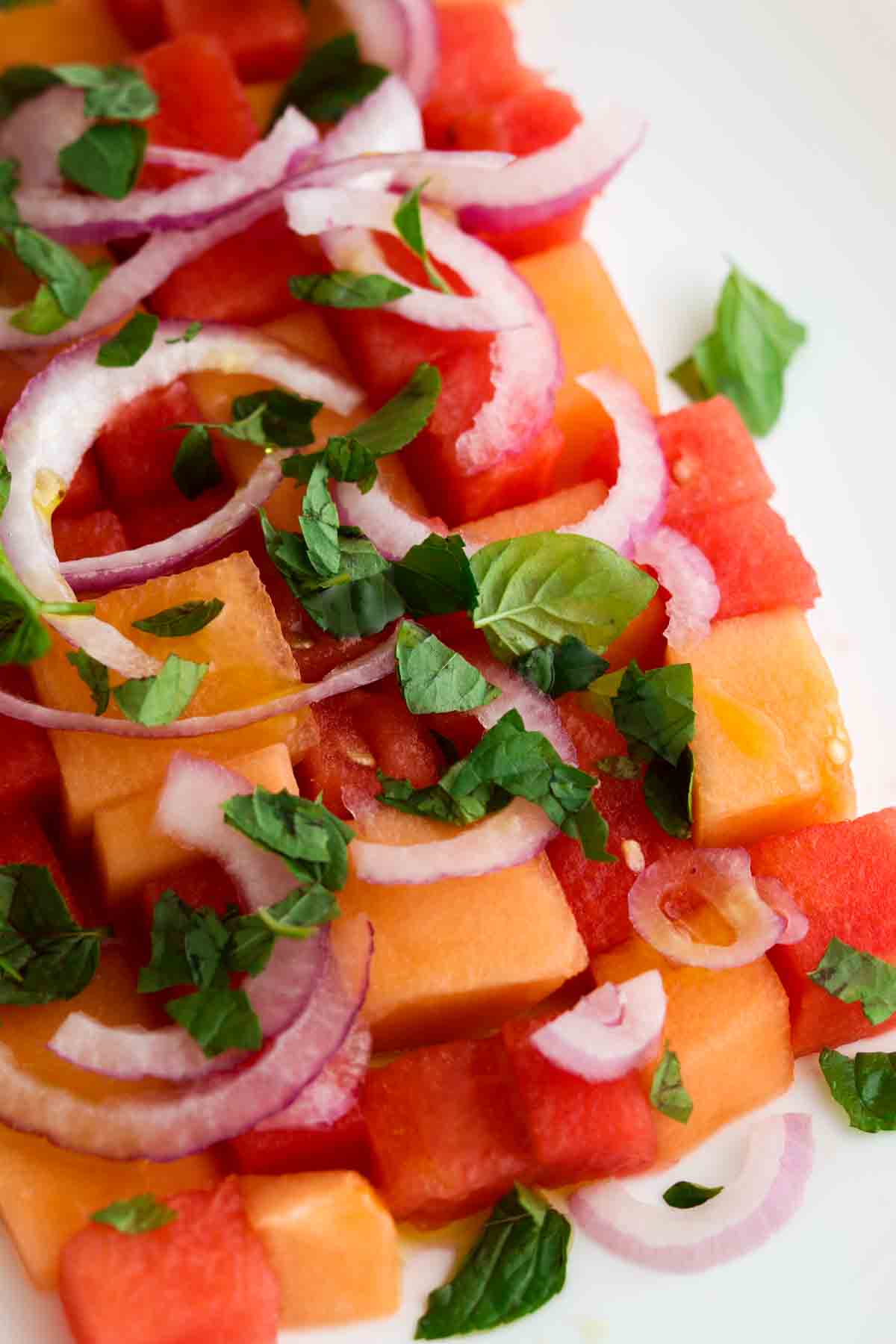 Melon salad with fresh mint on top on a white plate. 