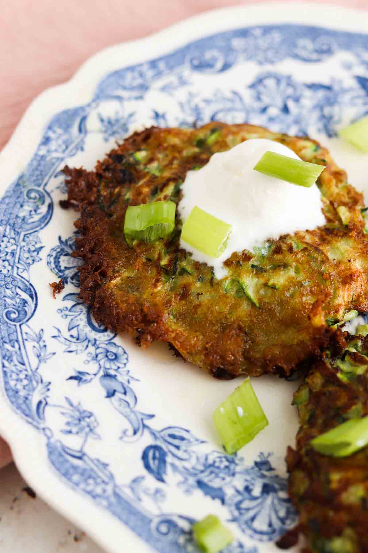 Zucchini patties on a plate with green onions, sour cream and pink napkin. 