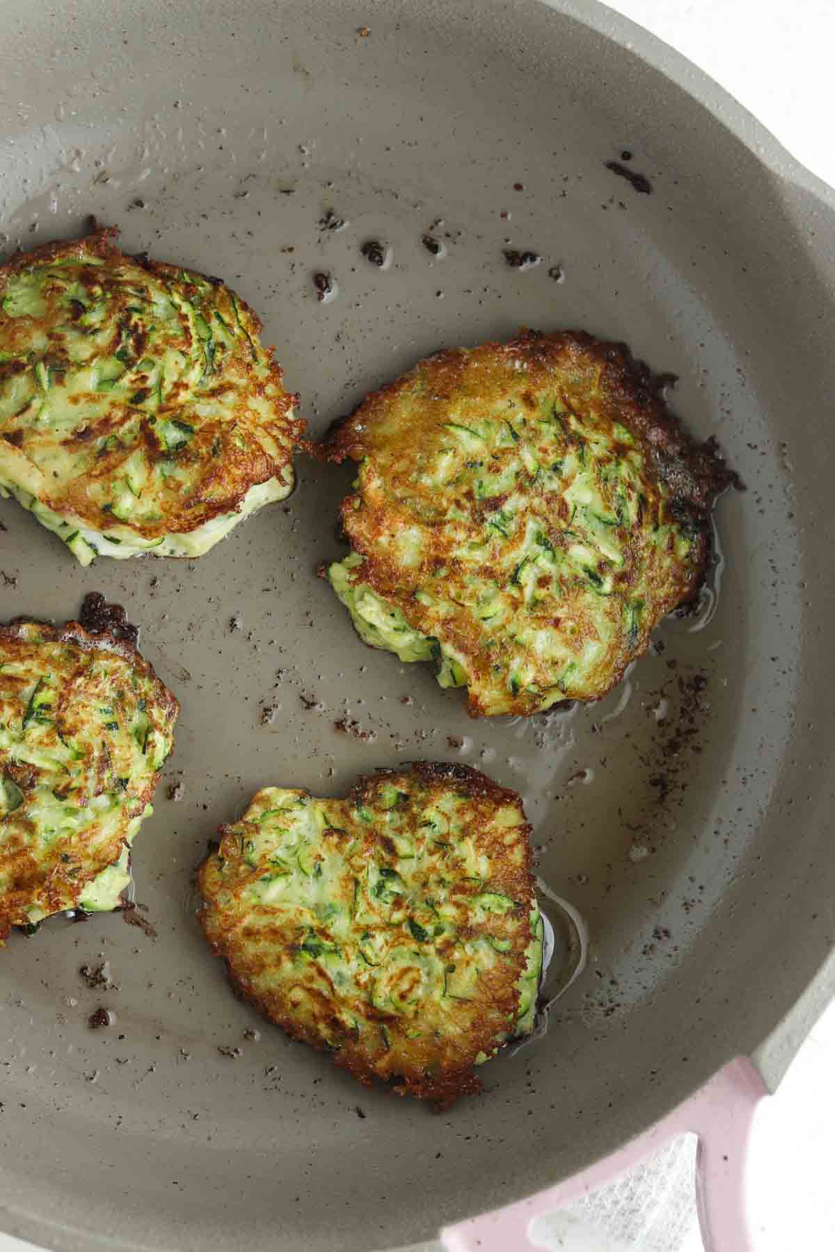 Zucchini patties scooped onto a frying pan. 